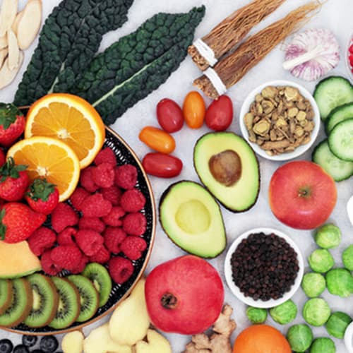 Looking down on a table filled with various different fruit and a bowl of oats representing a good anti-inflammatory diet option. There are also some vegetables like avocado which is also great for inflammation