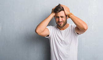 Handsome young man over grey grunge wall suffering from headache