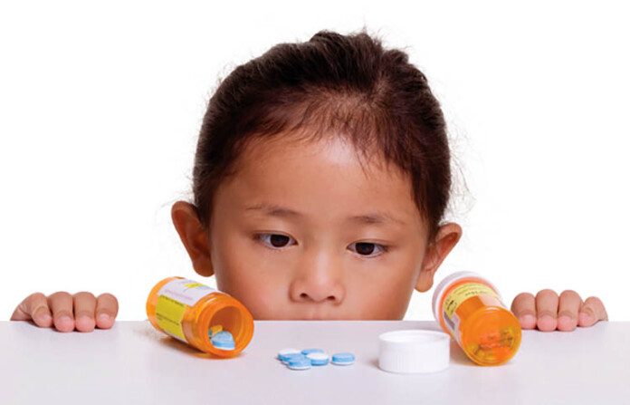 A young girl looks at a pile of pills that was left on a counter.
