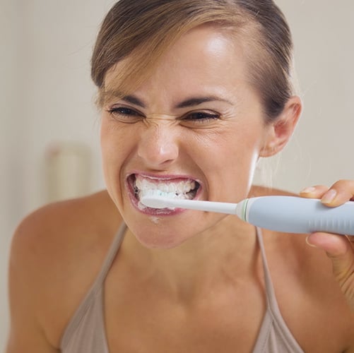 Young woman brushing teeth with grimace on face