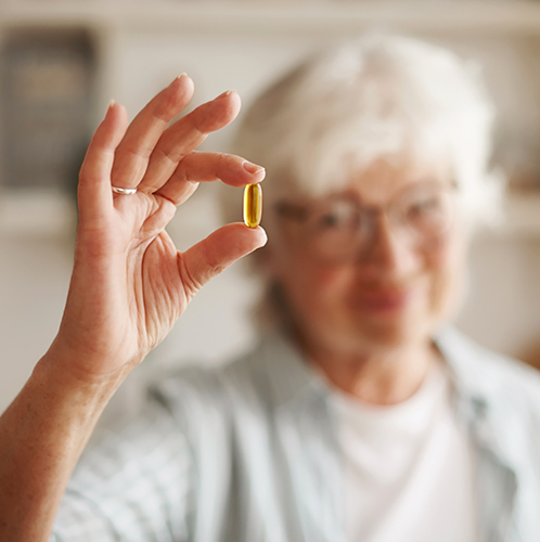 Food, nutrition, diet and health concept. Close up shot of elderly woman's hand holding fish oil or omega-3 polyunsaturated fatty acid supplement in shape of capsule, going to take one during lunch